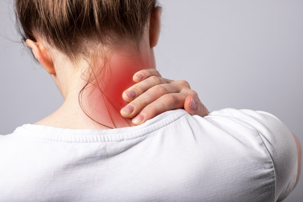 Woman in Sugar Land, seen from behind, holds her painful neck before her cervical disc replacement procedure