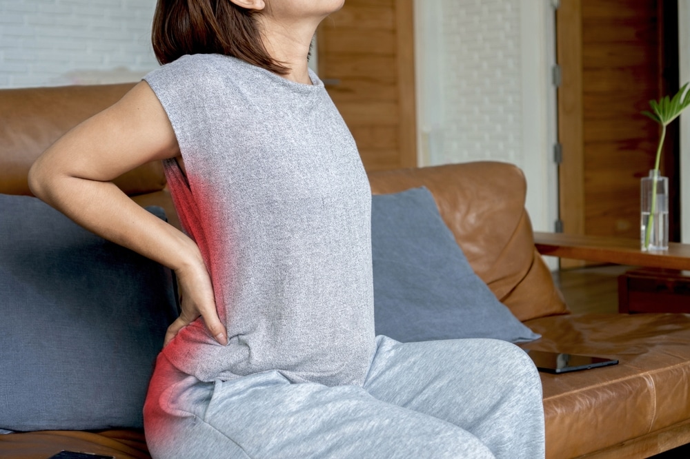 Woman in Sugar Land sits on a couch and holds her painful lower back, struggling with sciatica
