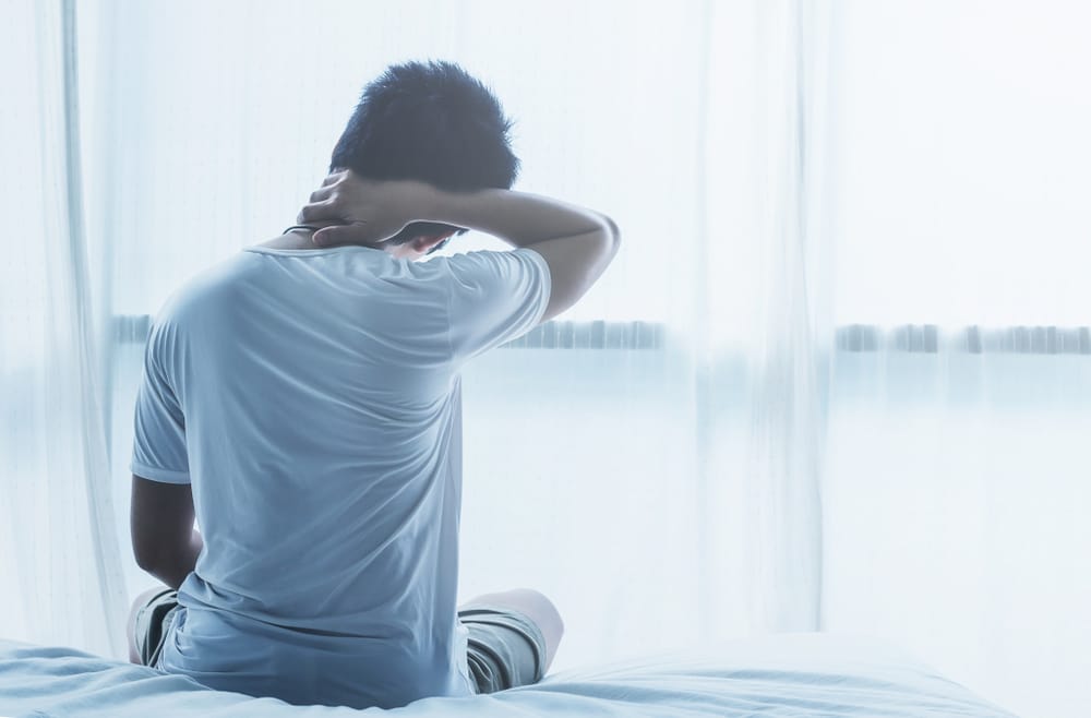 Person sitting on a bed holding their neck while comparing artificial disc replacement and fusion.