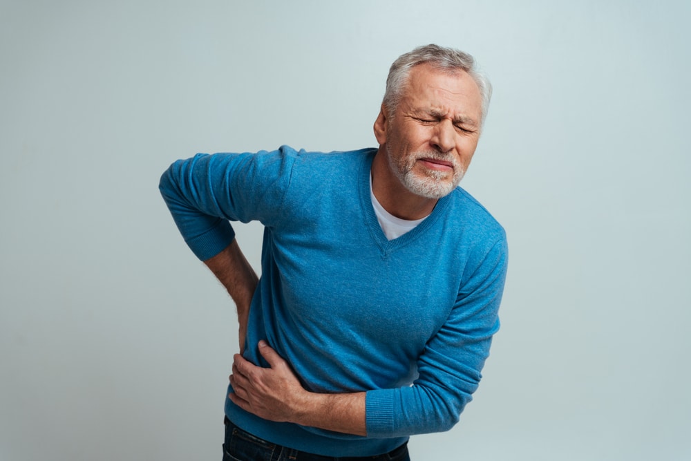 Man clutching his lower back in pain from possible spinal stenosis or herniated disc symptoms.