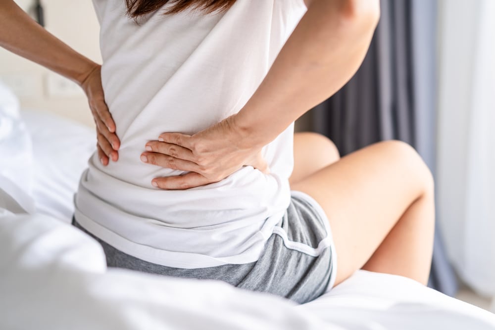 Person sitting on a bed holding their lower back while researching minimally invasive spine surgery.