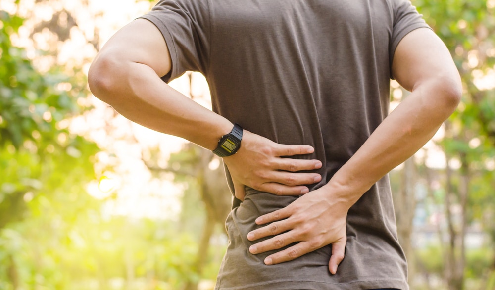 Person pressing on their lower back with pain related to spondylolisthesis symptoms.